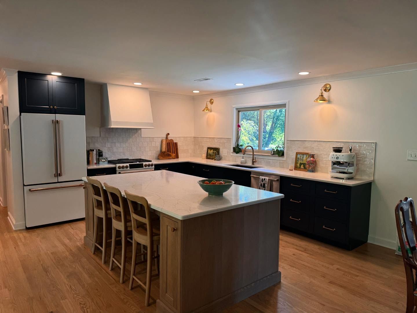 Modern kitchen with island, white countertops, black cabinets, and wooden floors.