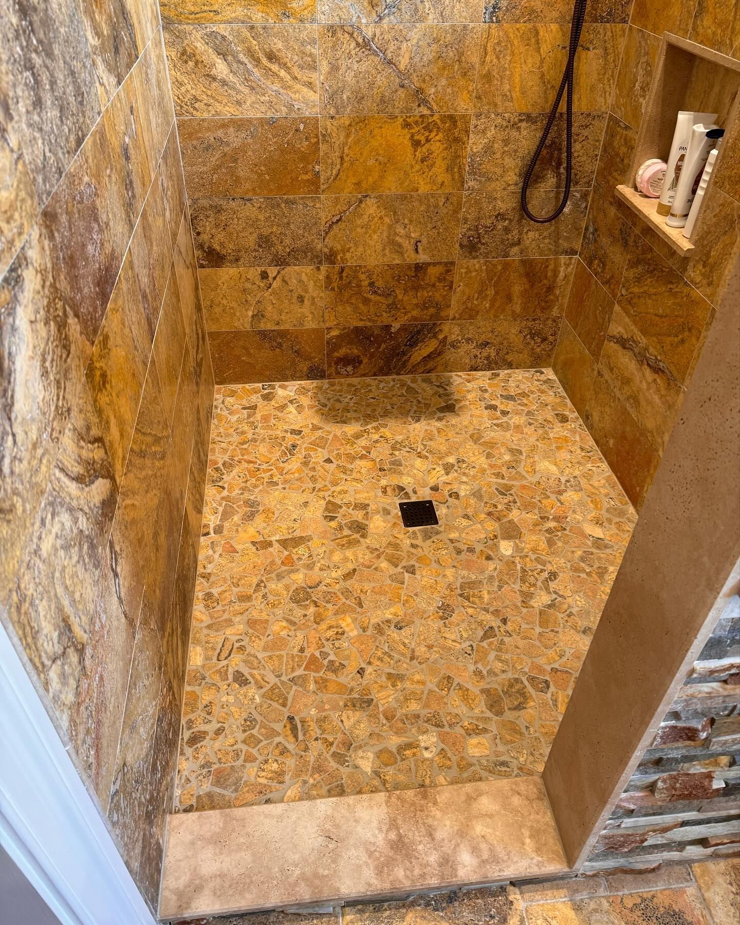 Shower with brown stone tile walls and floor, a built-in shelf, and dark drain.