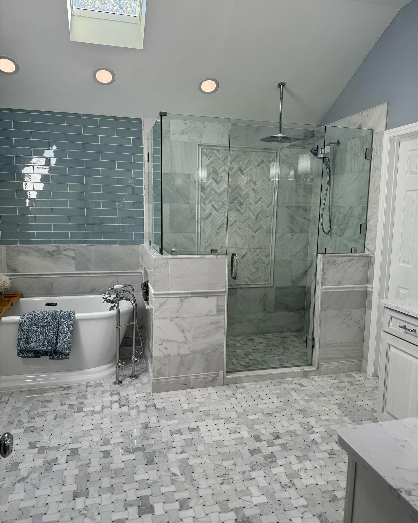 Luxurious bathroom with marble tile and glass shower. Features a soaking tub and blue accent wall.