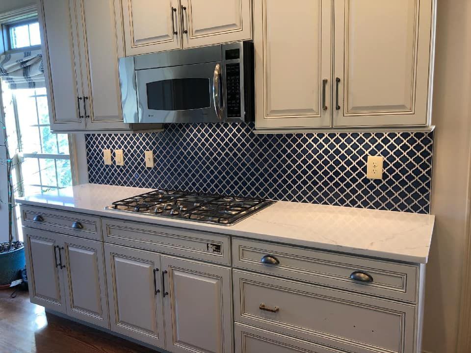 Kitchen with light gray cabinets, white countertops, blue tile backsplash, and stainless steel microwave and stovetop.