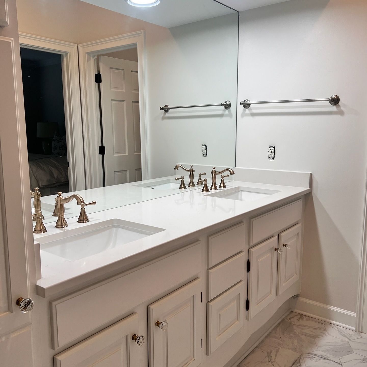 White double-sink vanity with silver fixtures and a large mirror in a bathroom setting.