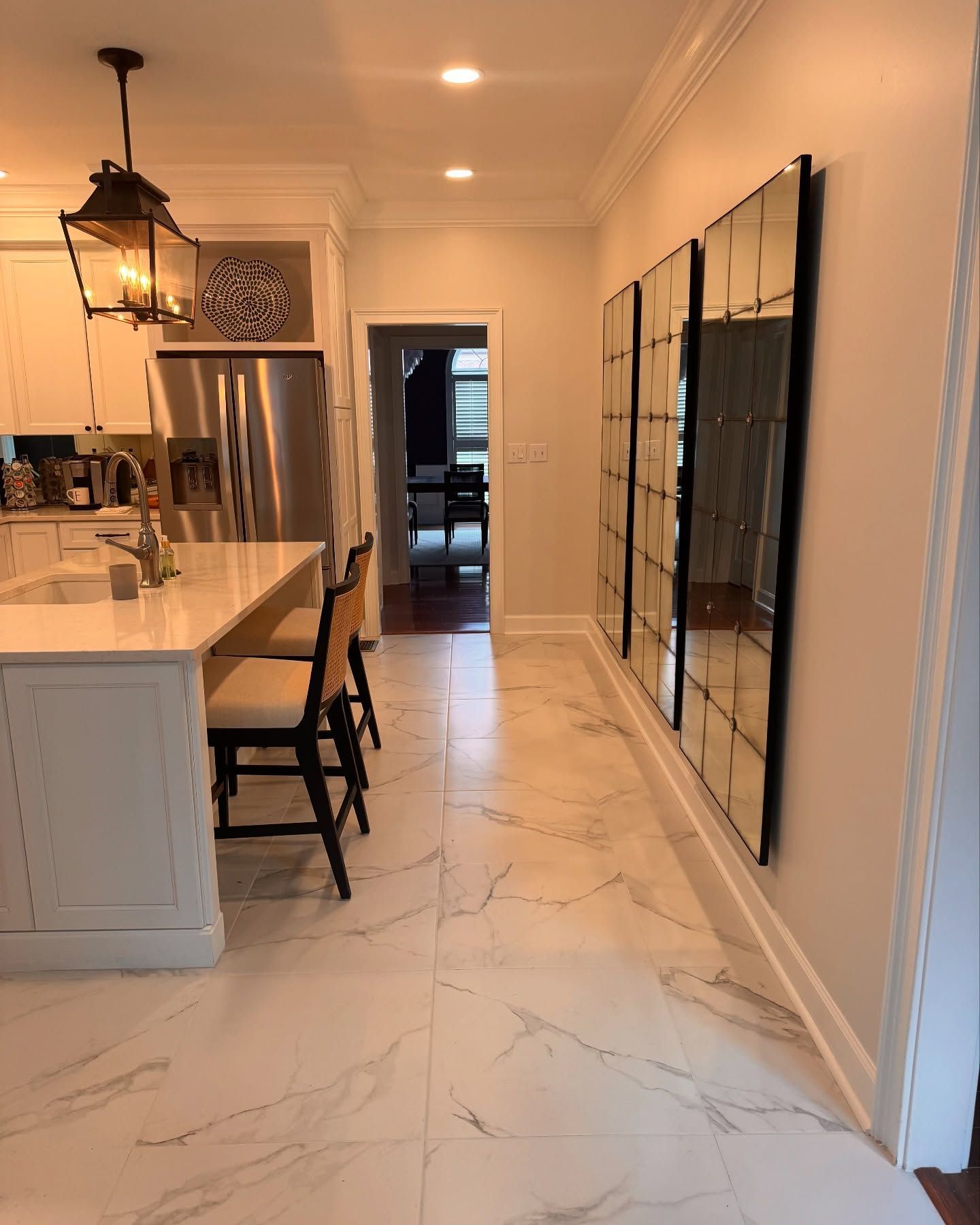 Kitchen with marble floor, white cabinets, island with stools, and mirrored wall panels.