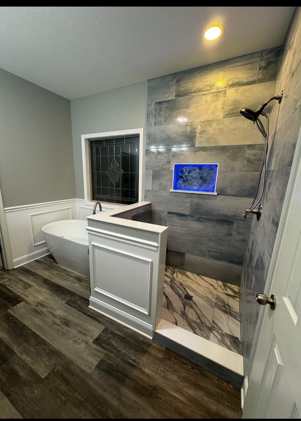 Bathroom with gray tiled shower, freestanding tub, and wood-look flooring.