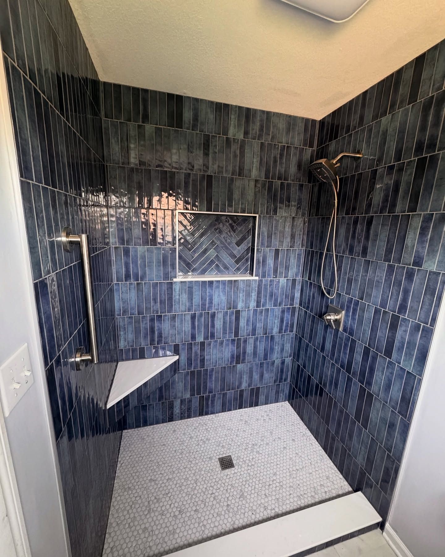 Blue tiled shower with a white tiled floor and shower bench.