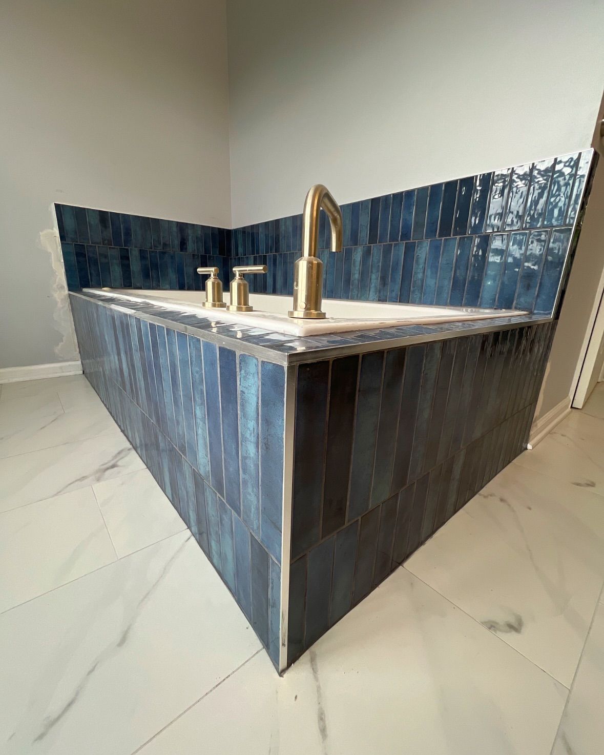 Blue tiled bathtub with gold fixtures, in a bathroom with white marble floors.