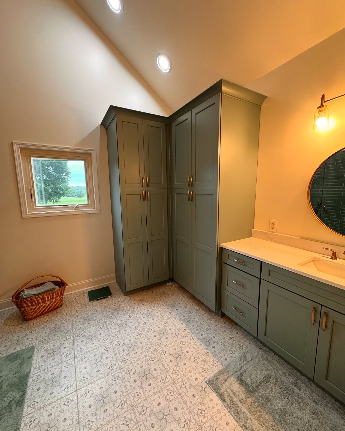 Bathroom with sage green cabinets, light countertops, small window, and patterned tile floor.