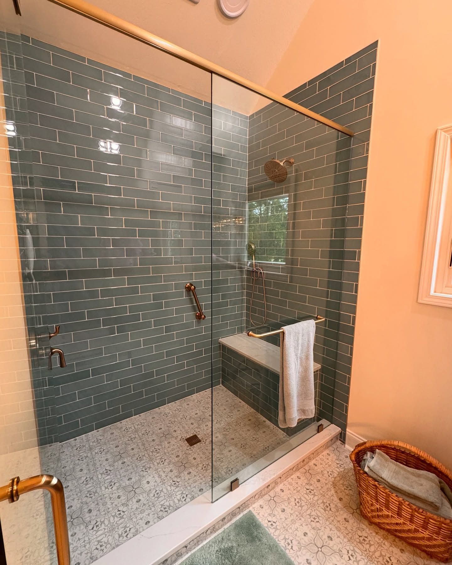 Shower with blue-gray tiled walls, glass doors, gold fixtures, and a speckled floor.