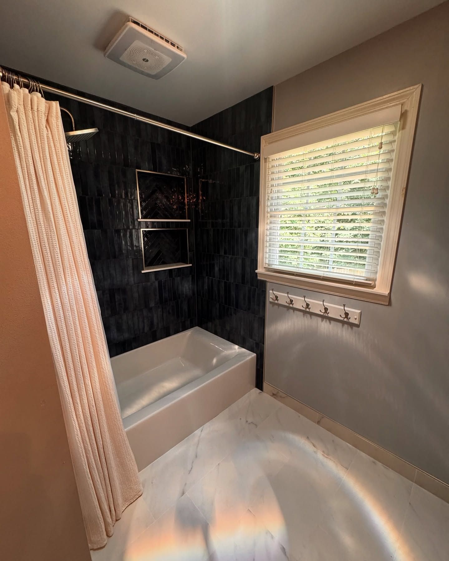 Bathroom with black tiled shower, white tub, window with blinds, and pink shower curtain.