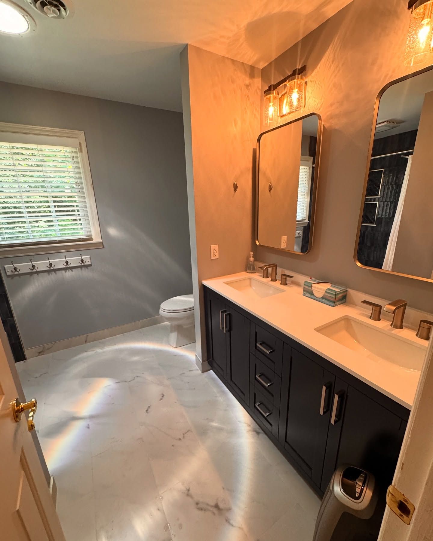 Bathroom with dark wood vanity, white countertops, two sinks, mirrors, and marble flooring.