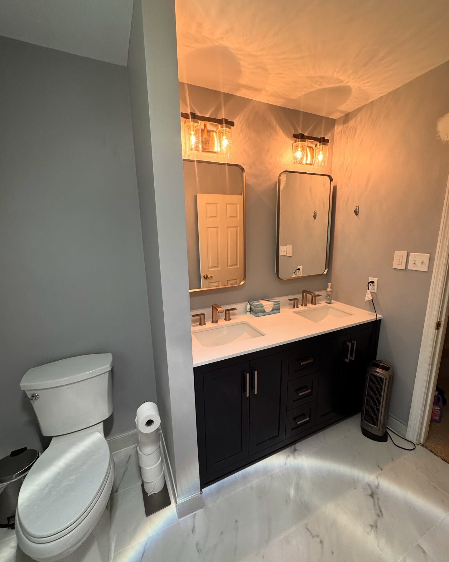 Bathroom with a white toilet, black vanity, and two mirrors on a gray wall.