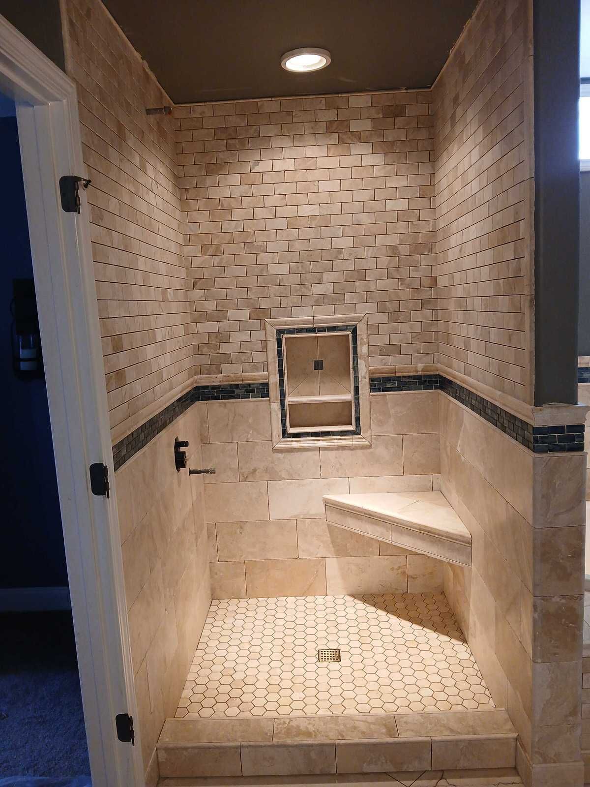 Shower with light beige stone tiles, built-in bench, recessed shelf, and dark trim.
