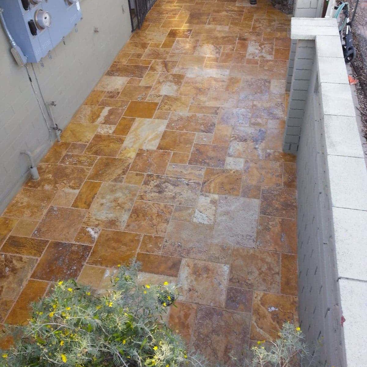 Travertine tile patio with gold and brown tones, bordered by a wall and building.