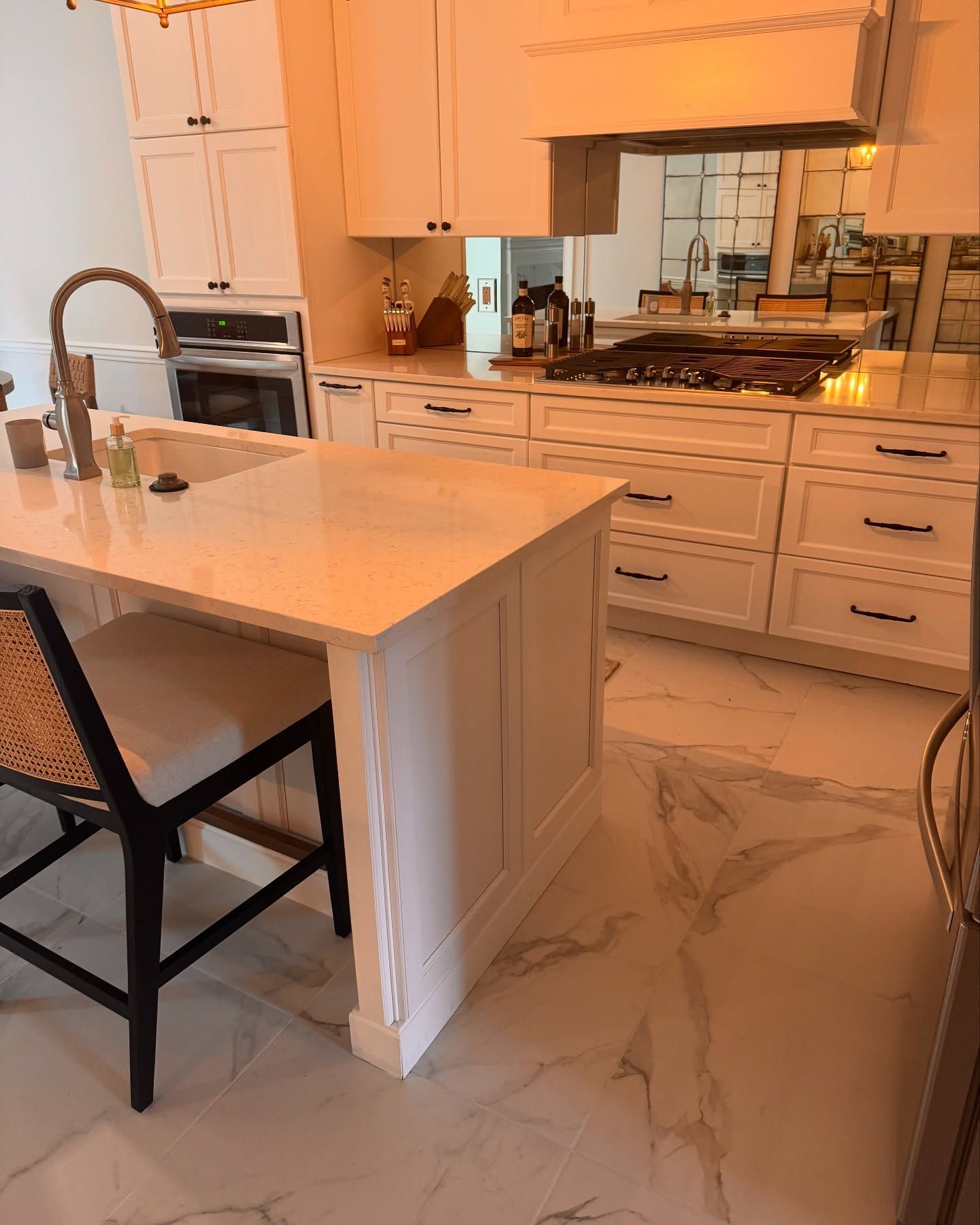 White kitchen with island, countertops, and cabinets. Light marble-patterned flooring. Barstool.