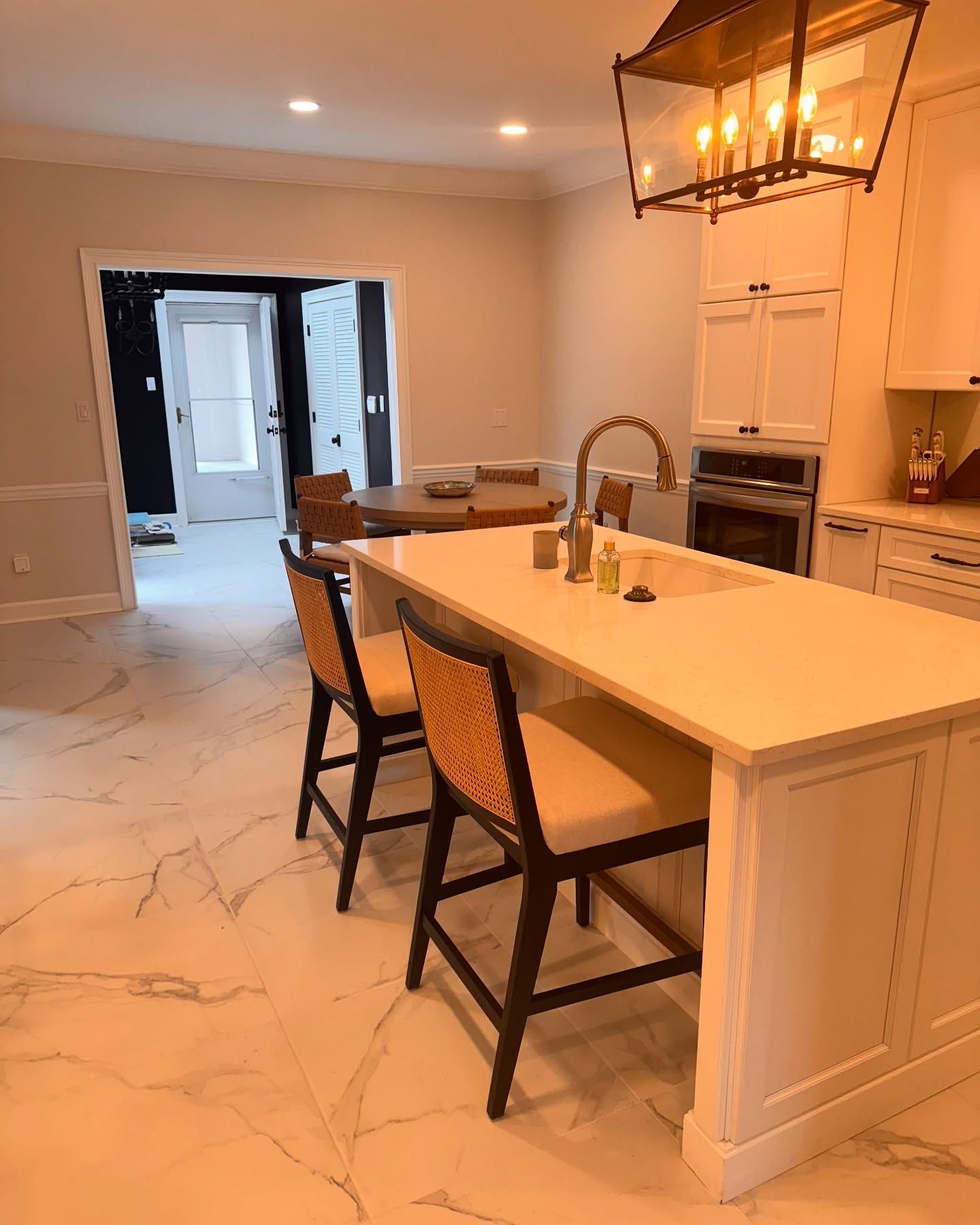 Modern kitchen with white cabinets, island, and seating; a dining area is visible.