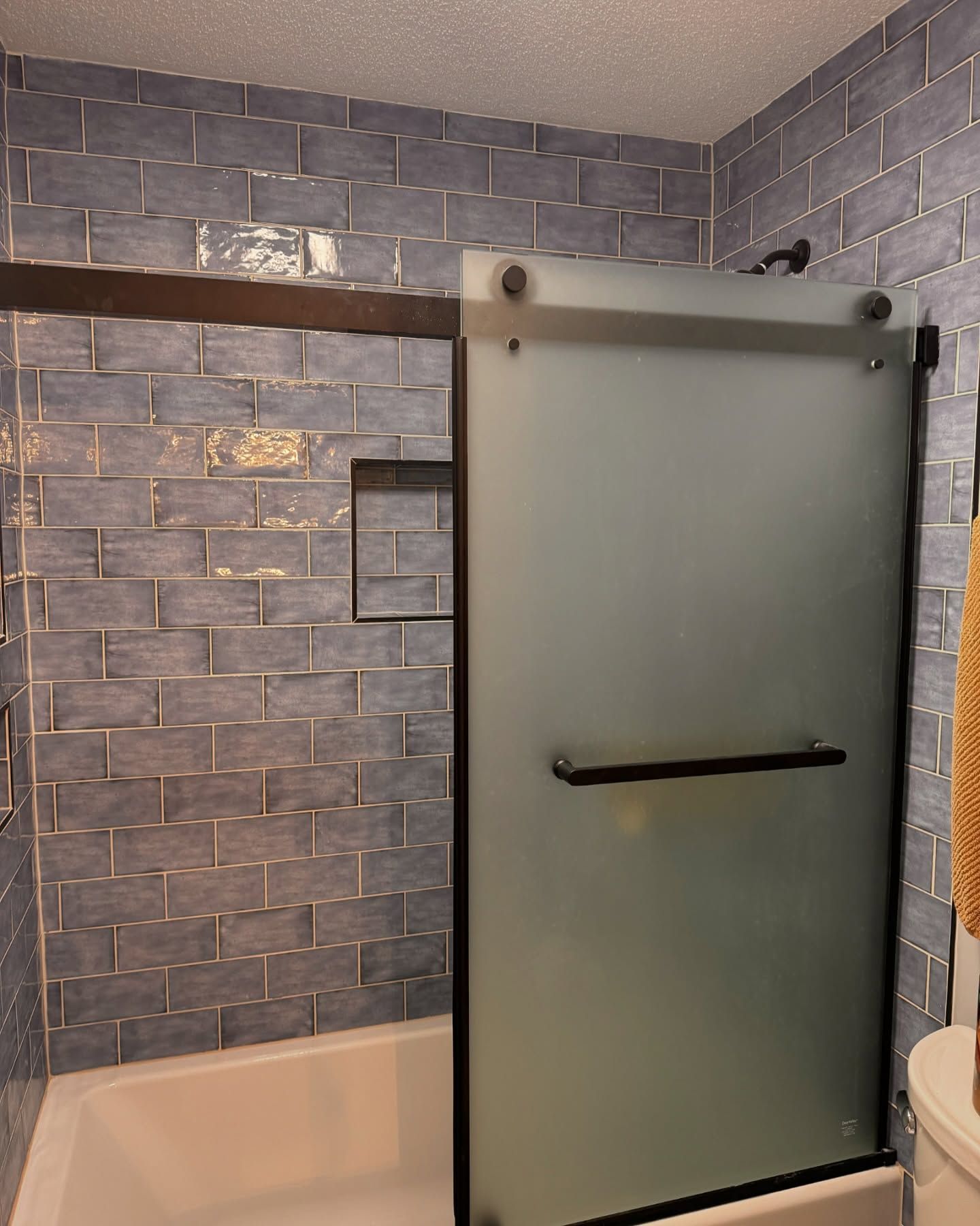 Blue tiled shower with a frosted glass door and black hardware.