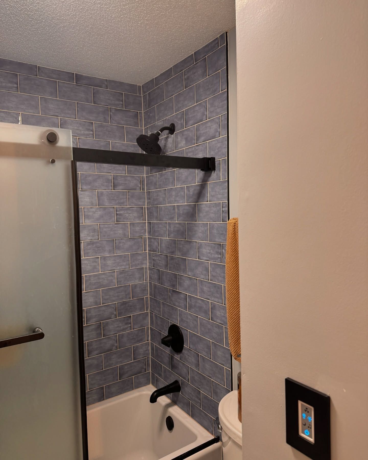 Bathroom with blue brick-patterned tile, black shower fixtures, glass door, and white tub.