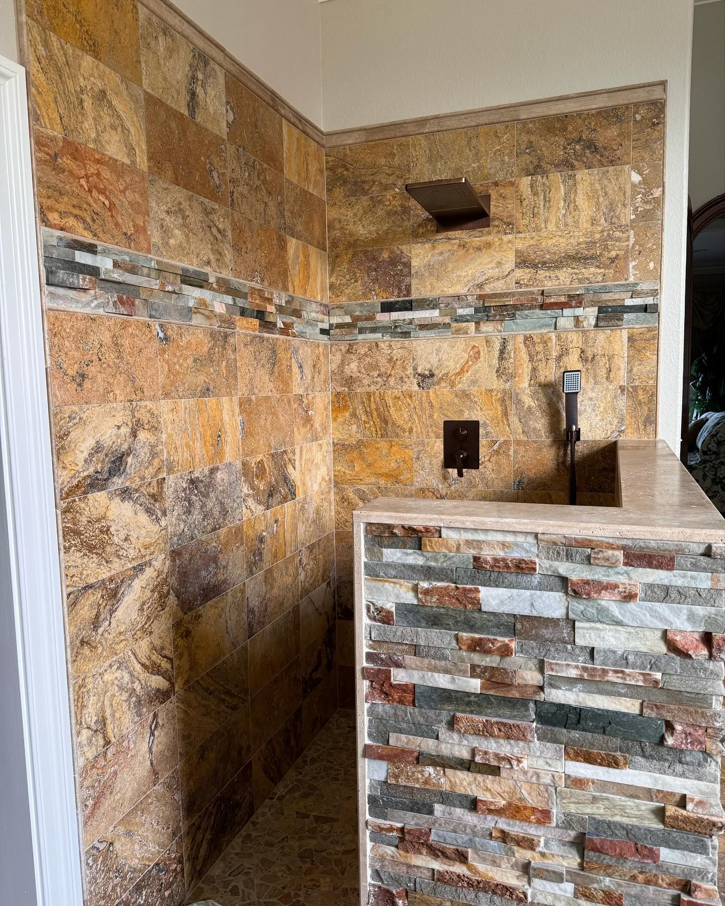 Shower stall with tan and multi-colored stone tiles. Built-in soap niche and shower head.
