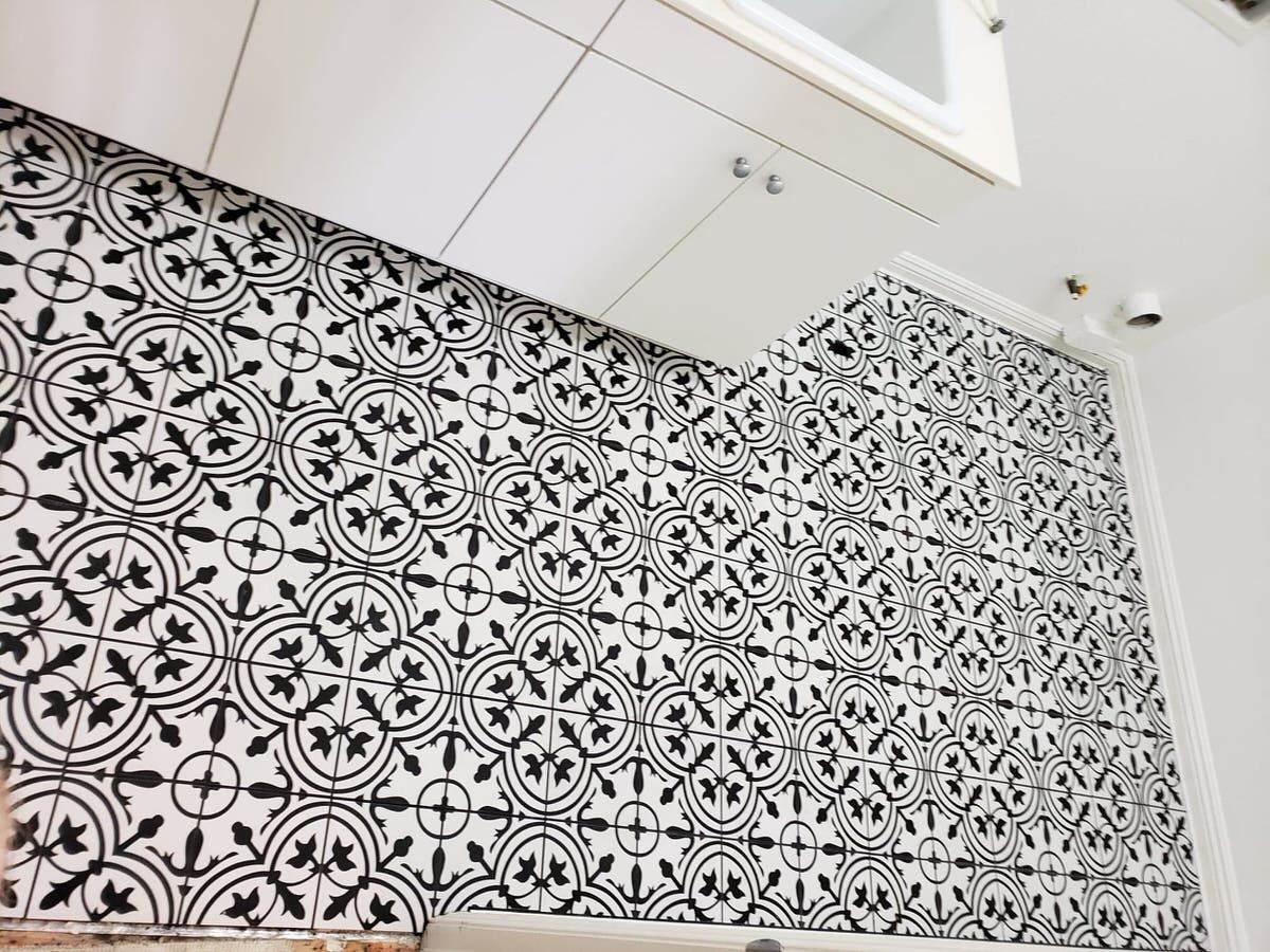 Black and white patterned tiles on a kitchen backsplash, white cabinet above.