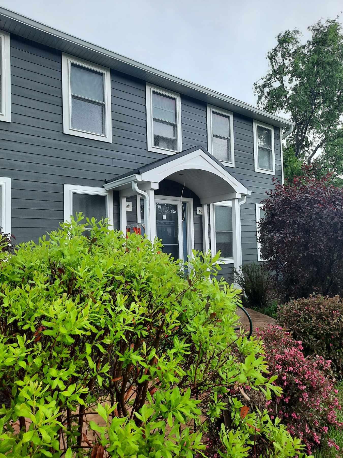Grey house with white trim and a bush in the front yard