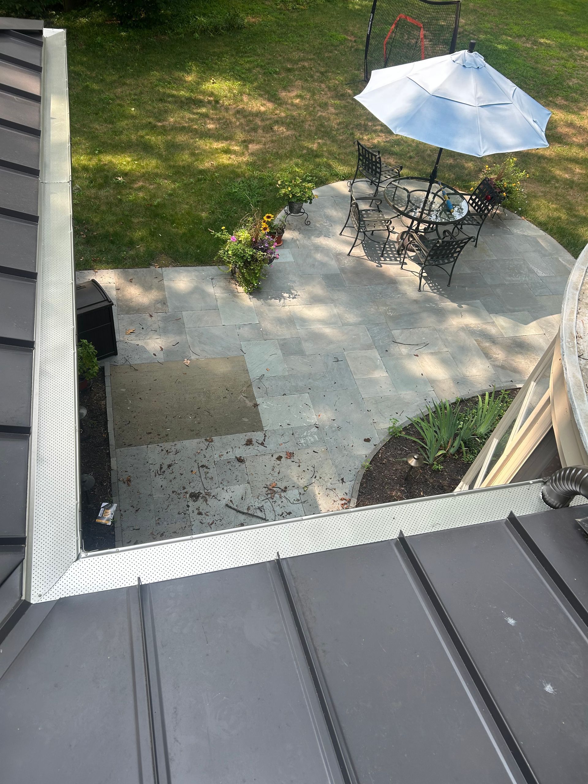 Overhead view of a patio with a table, umbrella, and garden, seen from a dark roof.