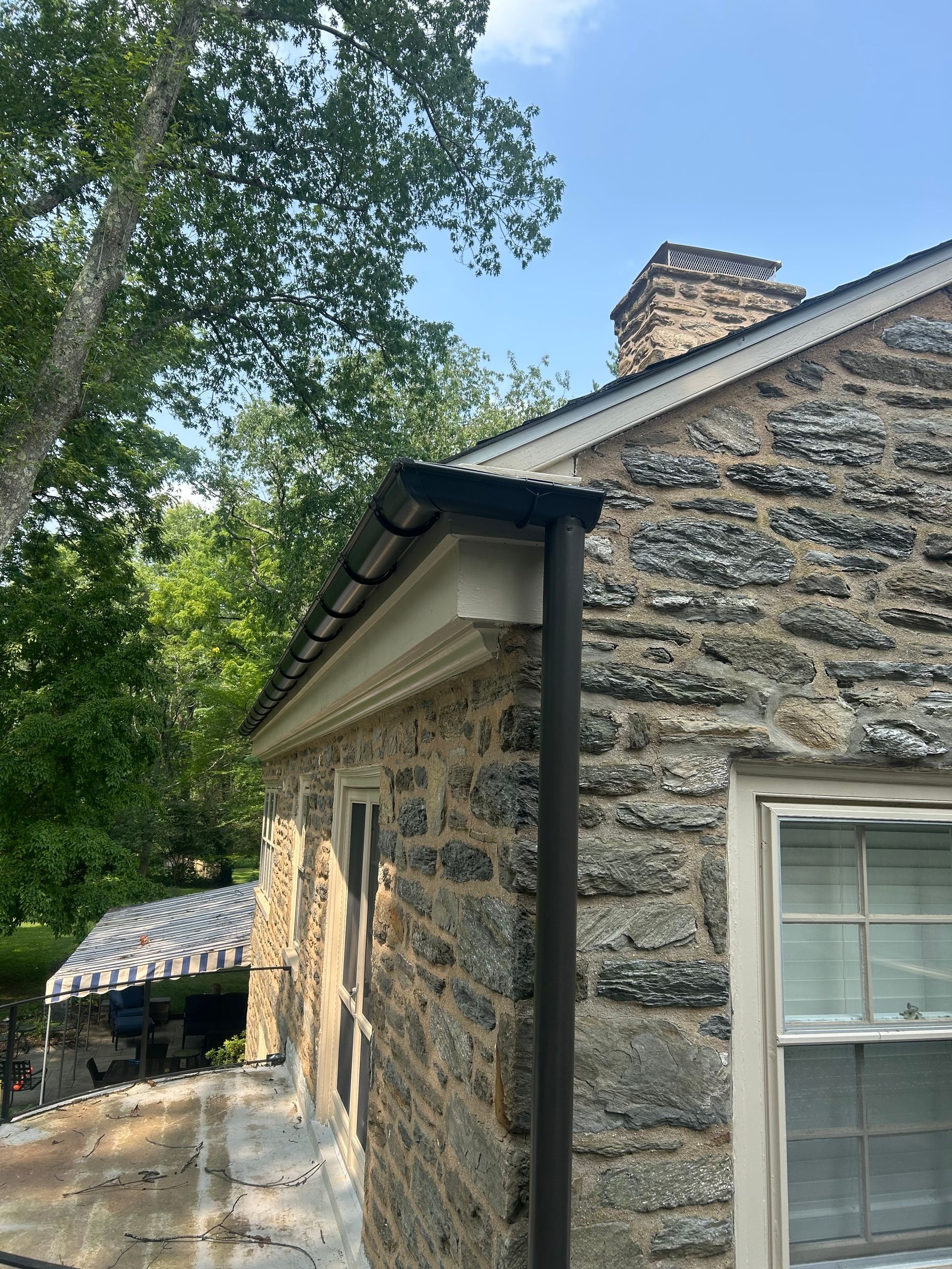 Stone building with black gutters, white trim, and a visible chimney against a blue sky.