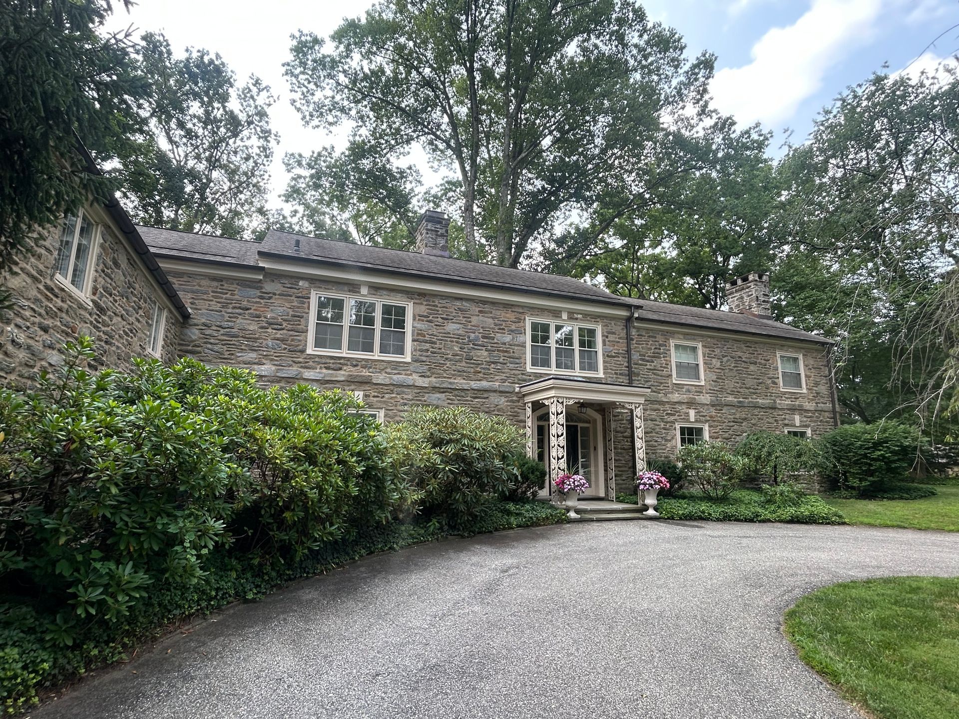 Stone house with gravel driveway and lush green landscaping.