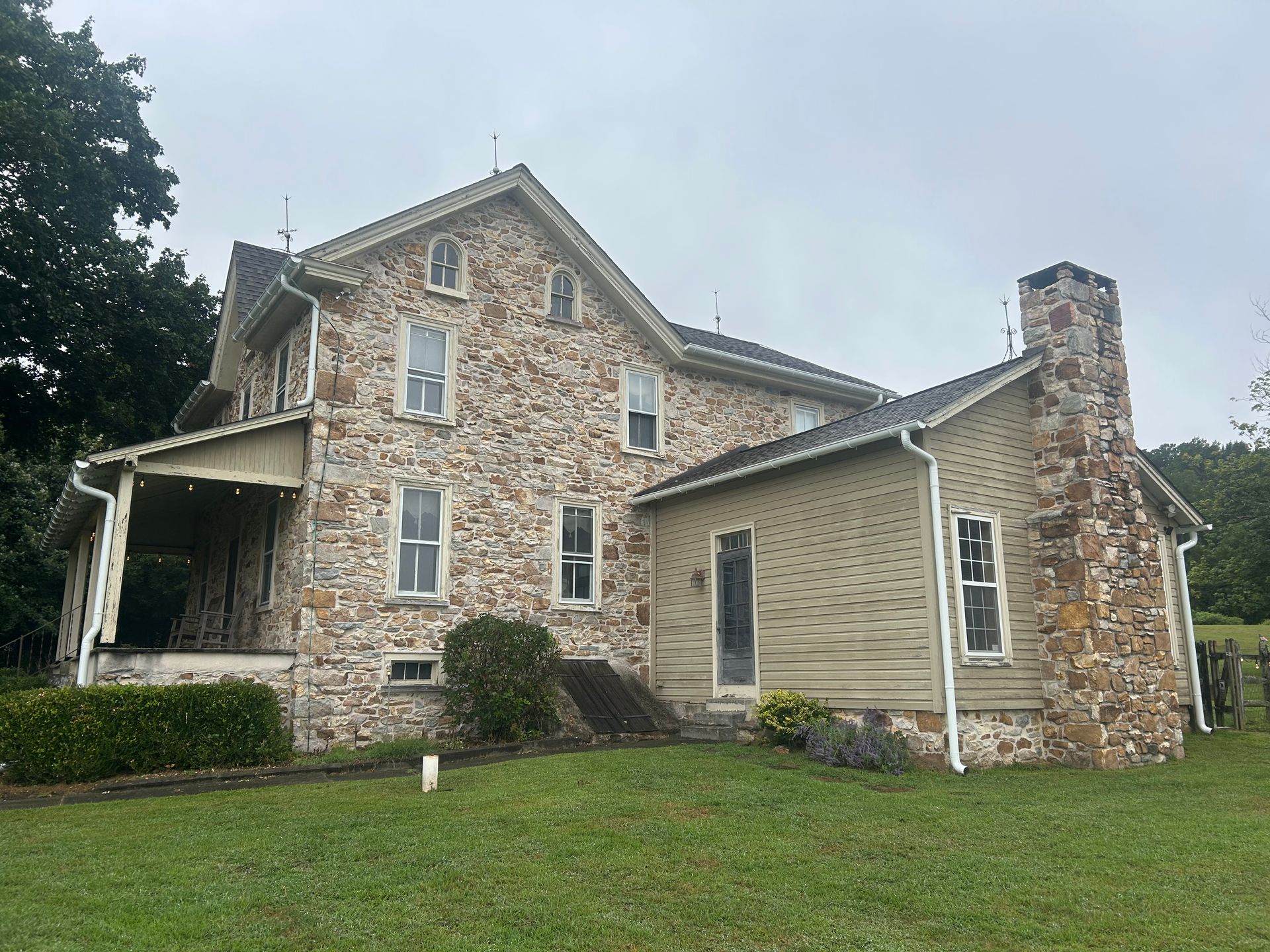 Stone house with porch, green lawn, and stone chimney under overcast sky.