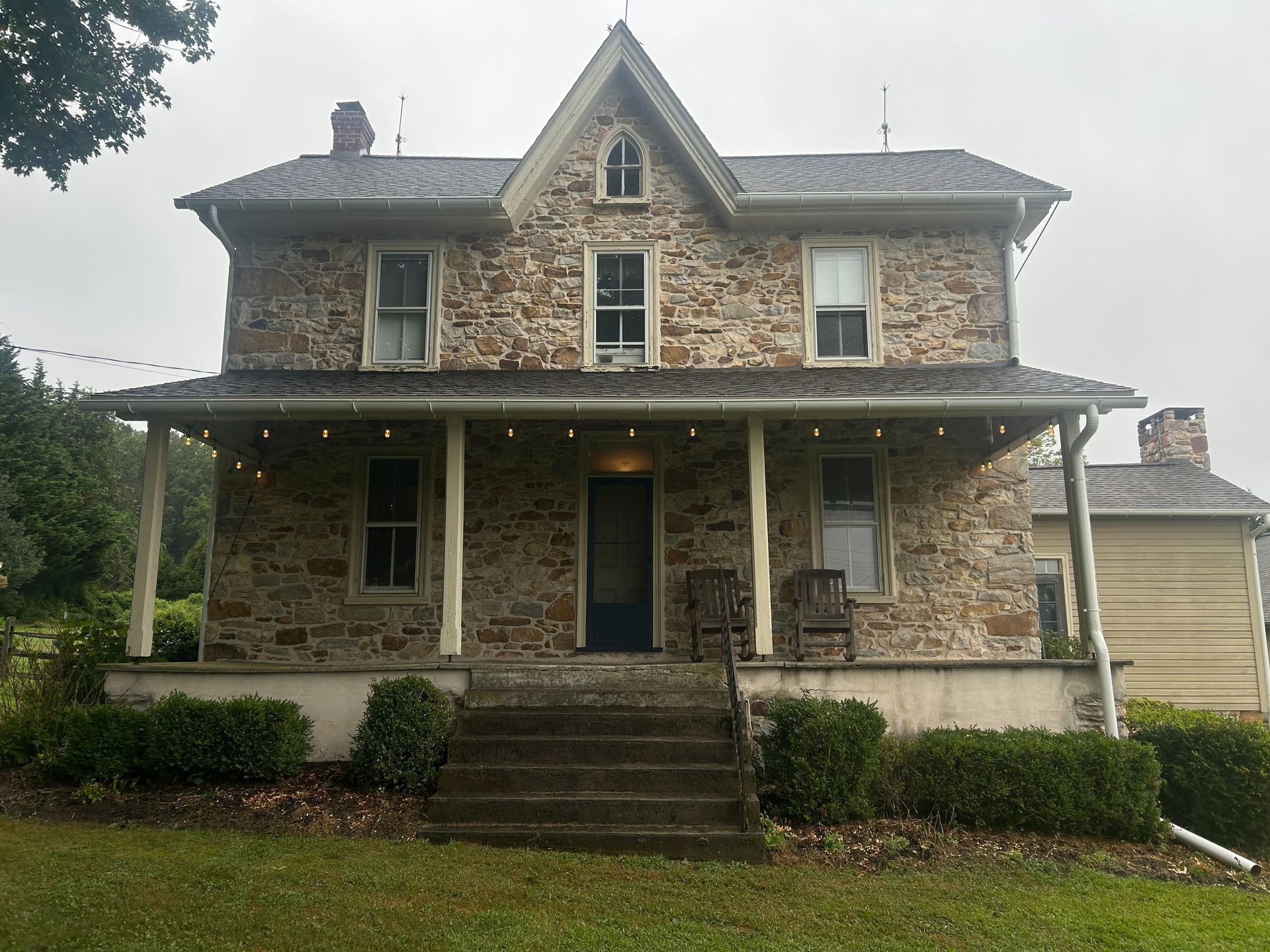 Stone house with porch, steps, and small front yard on a cloudy day.