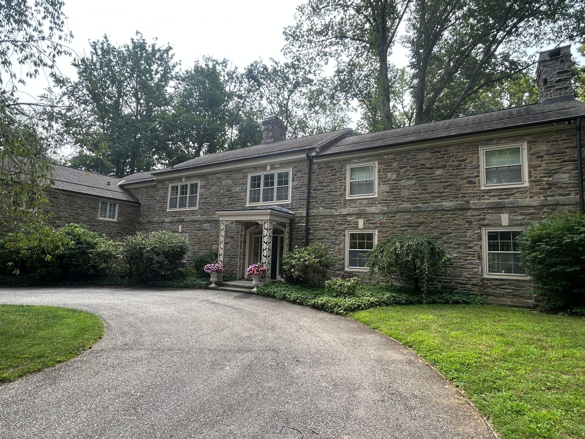 Stone house with a long driveway, surrounded by trees and green grass.