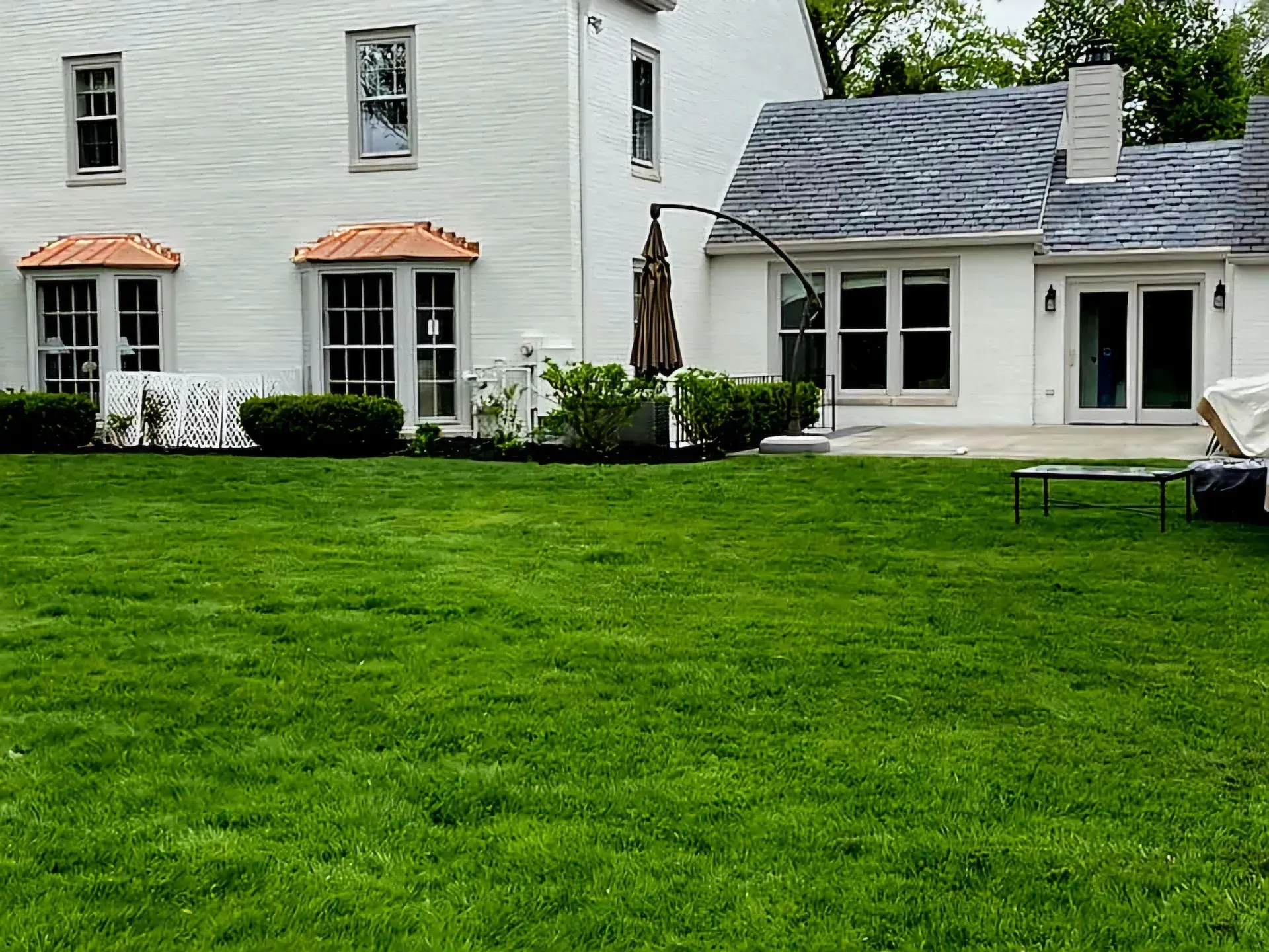 White house with a green lawn, patio doors, and a smaller attached section with gray shingles.