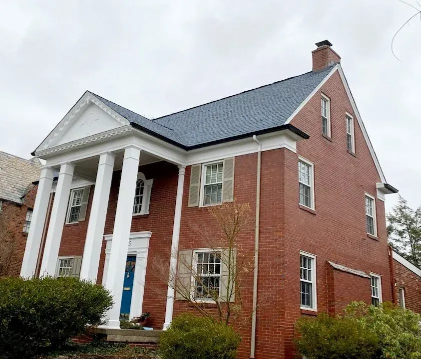 Red brick house with white columns, blue front door, and dark gray roof.