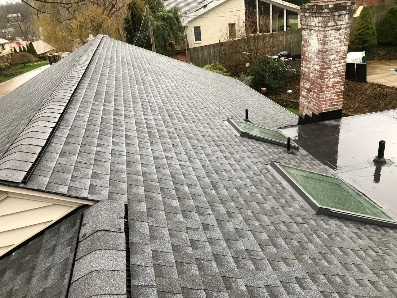 Snow-dusted shingled roof with two skylights and a brick chimney on a residential house