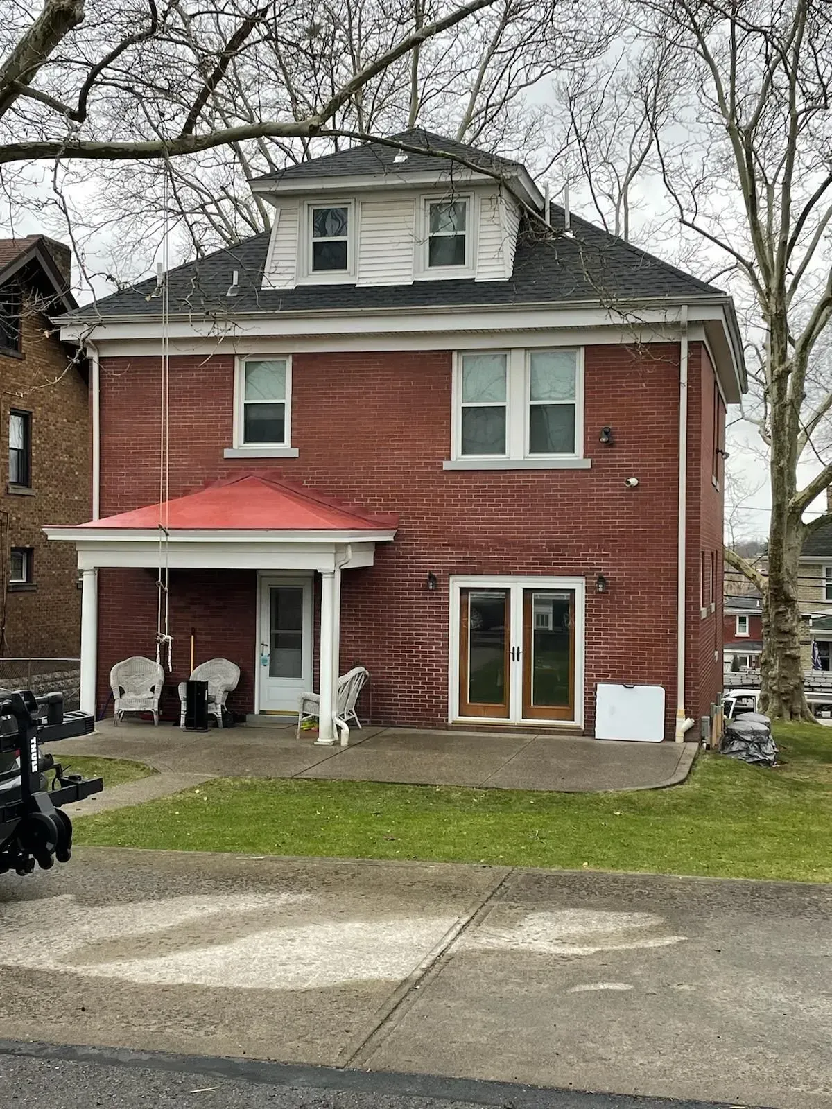 Red brick two-story house with white trim and front porch, viewed from across the street.