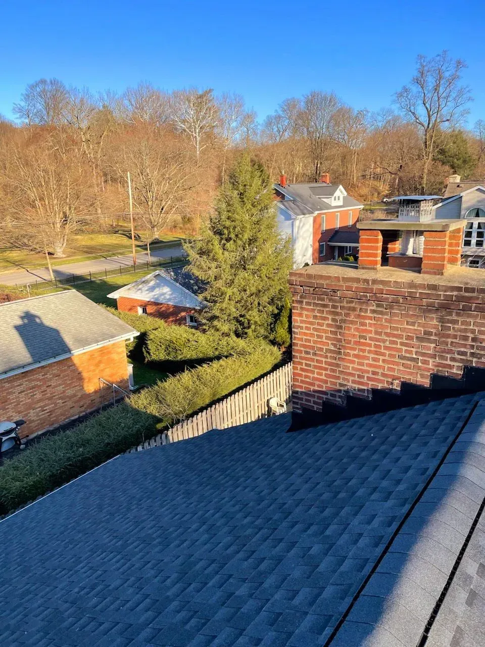 Rooftops and brick chimneys overlooking a wooded hillside in bright sunlight