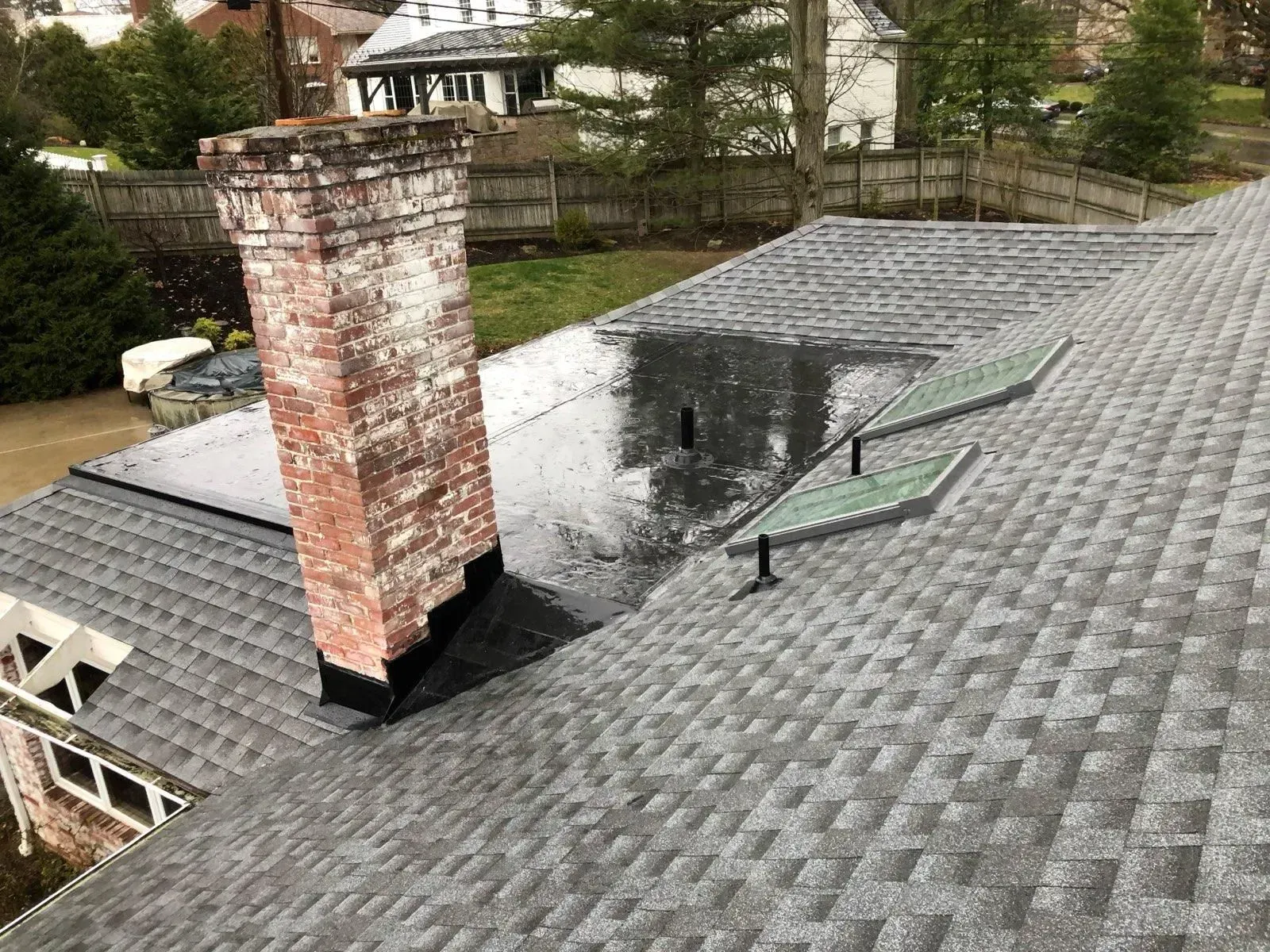 Flat shingled roof with a brick chimney and a dark wet patch near the center.