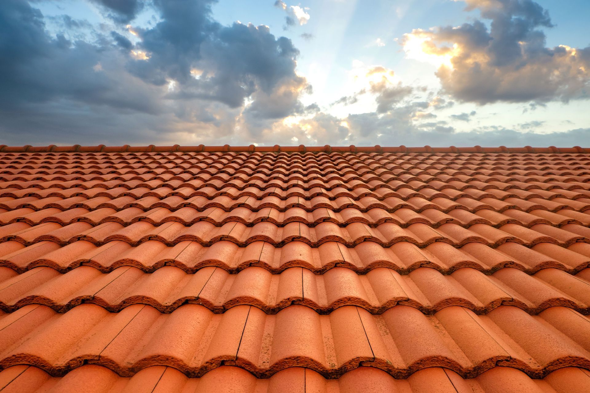 Orange terracotta roof tiles stretching toward a cloudy sunset sky