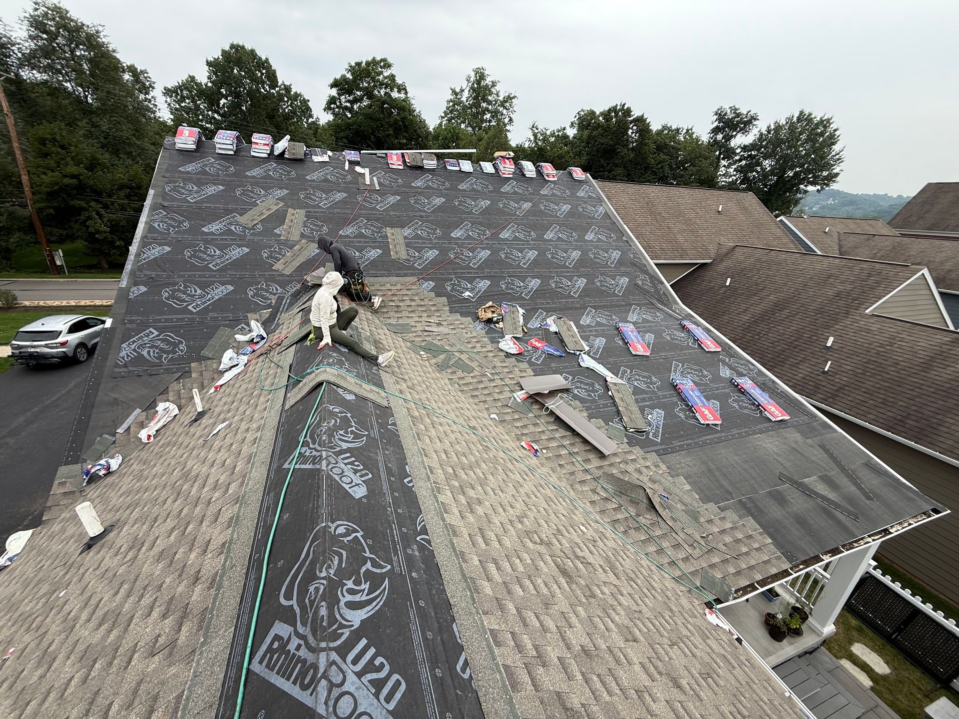 Roof under repair with dark shingles, roofing materials, and workers on a sloped residential house