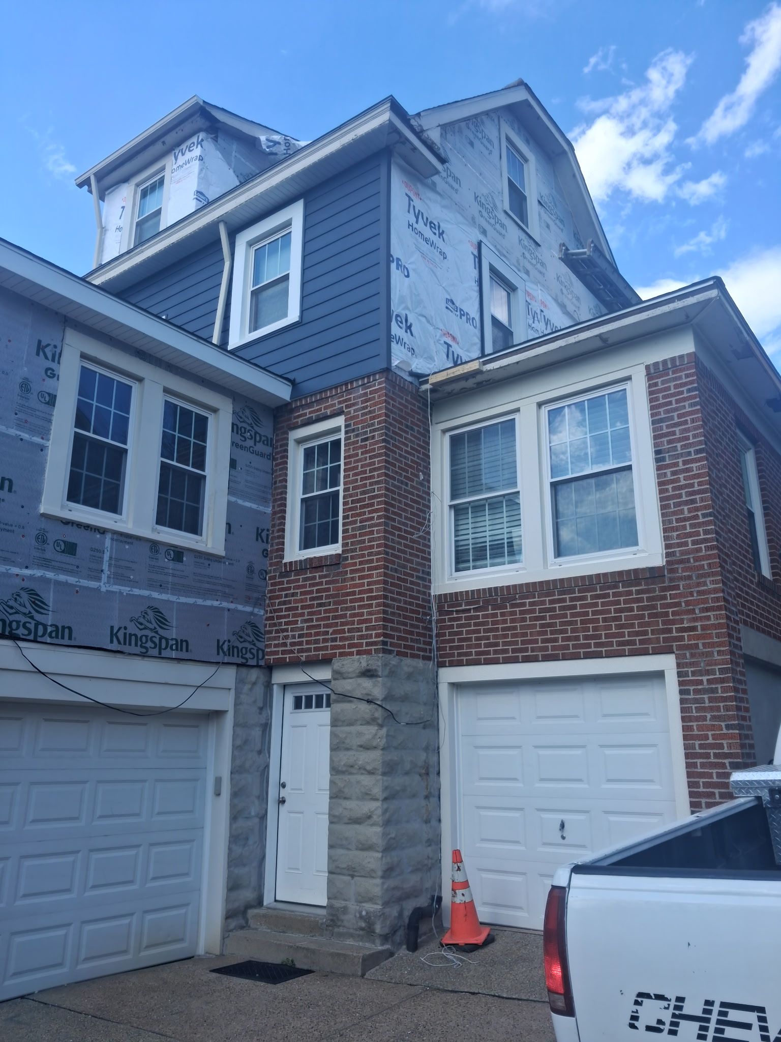 Three-story townhouse with garage doors and a red traffic cone in the driveway