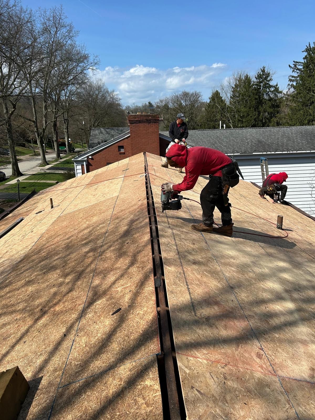 Workers installing roofing underlayment on a steep rooftop on a sunny day