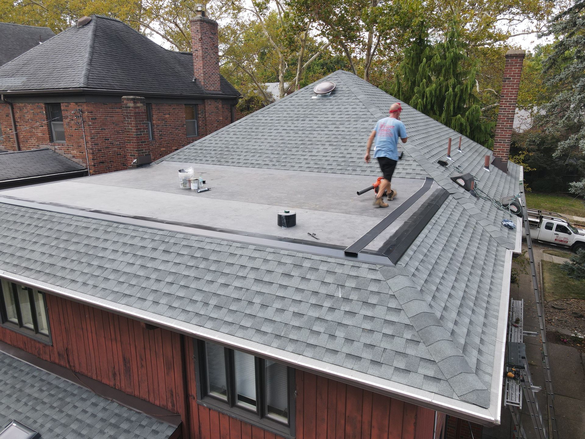 Worker inspecting a gray shingled roof on a brick house