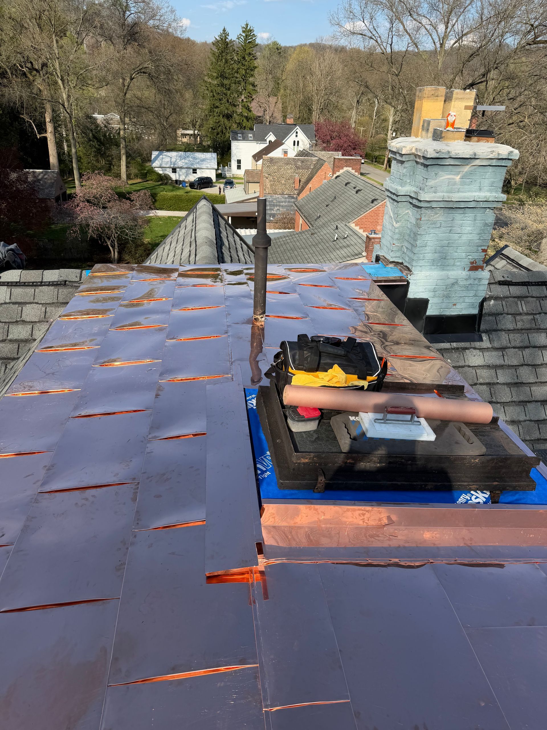Roofer repairing a slate roof with blue tarp, tools, and chimney in a residential neighborhood