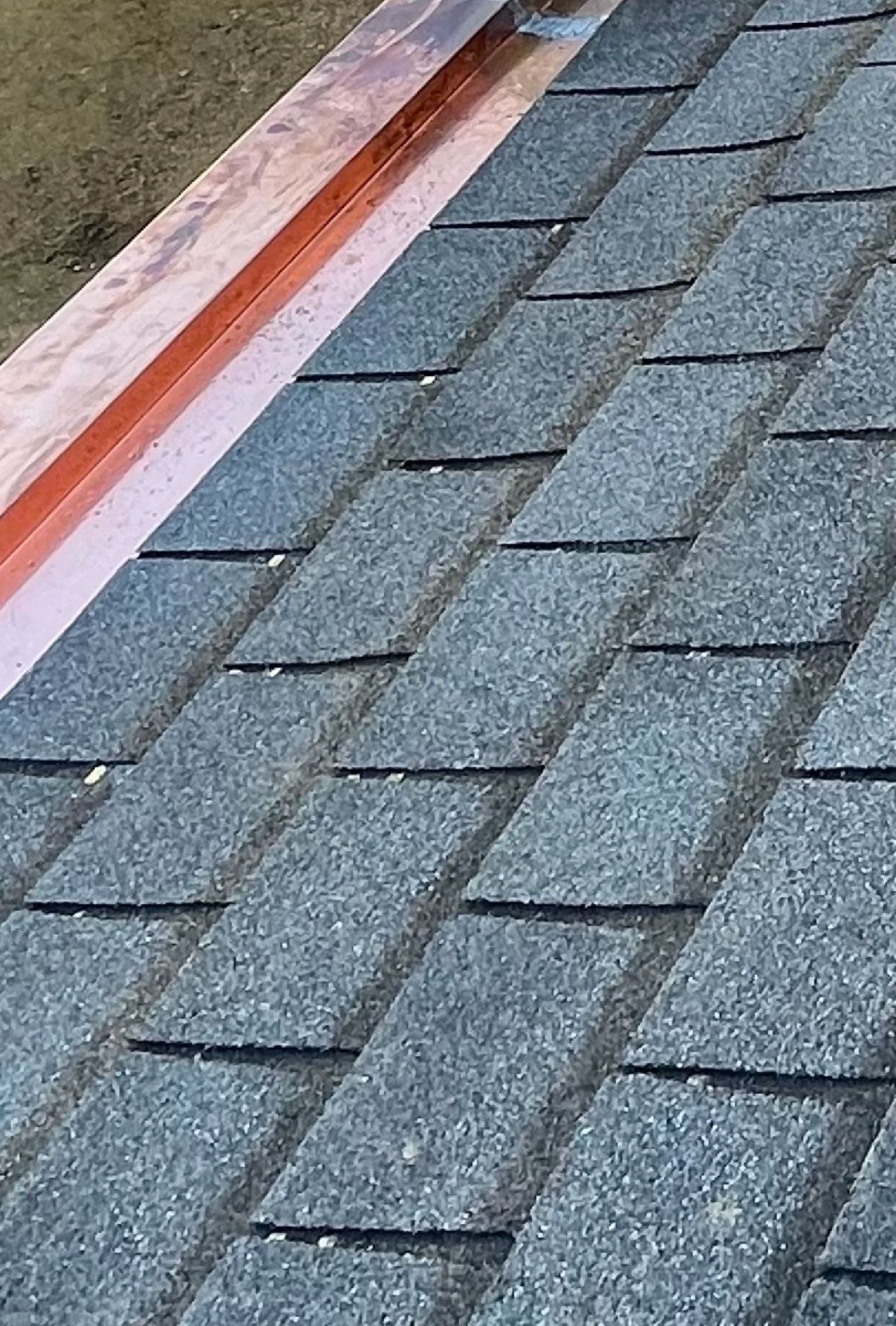 Gray asphalt roof shingles beside a rust-streaked white metal edge