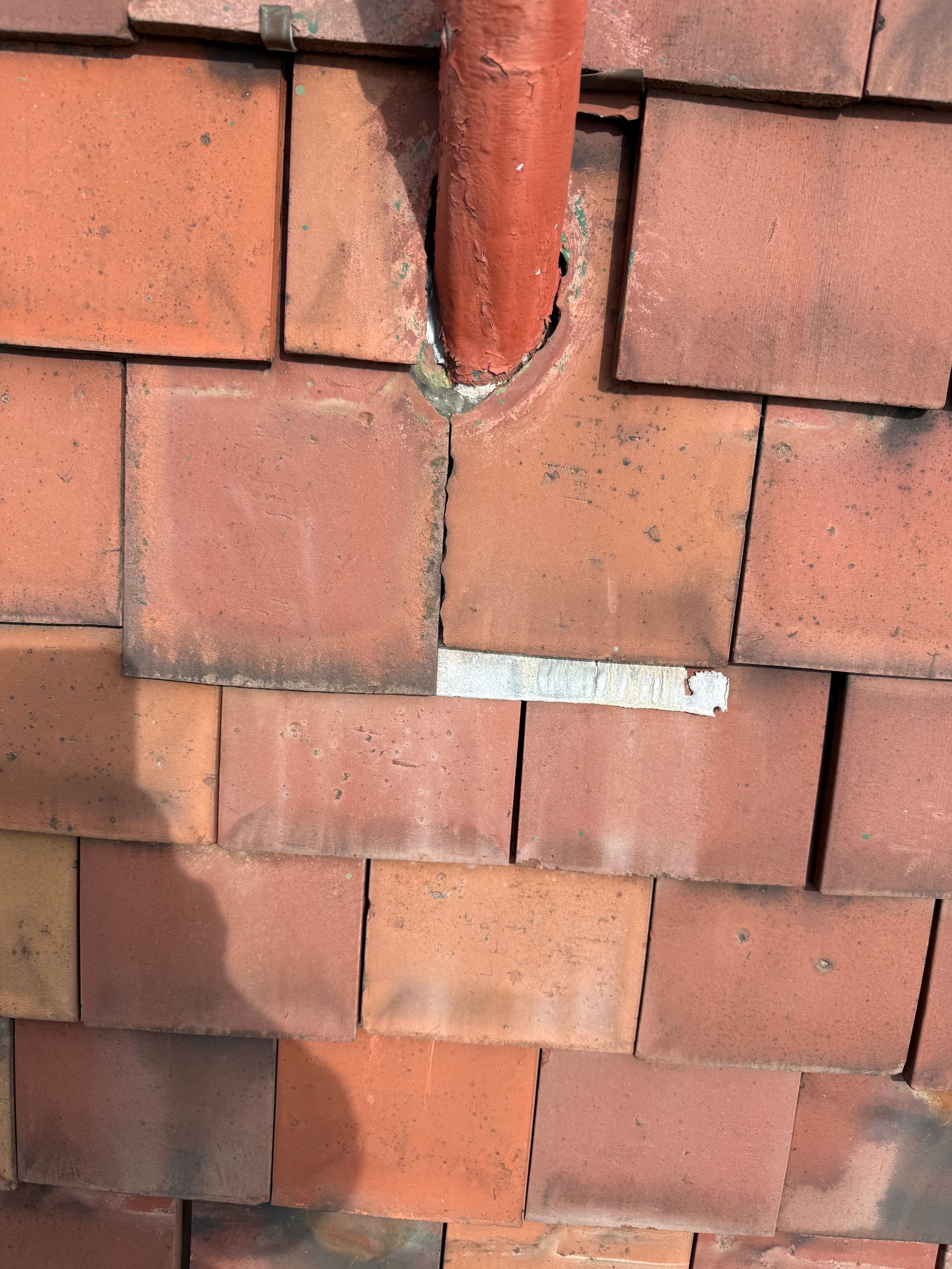 Close-up of red brick wall with a vertical pipe and a small patch of white repair mortar