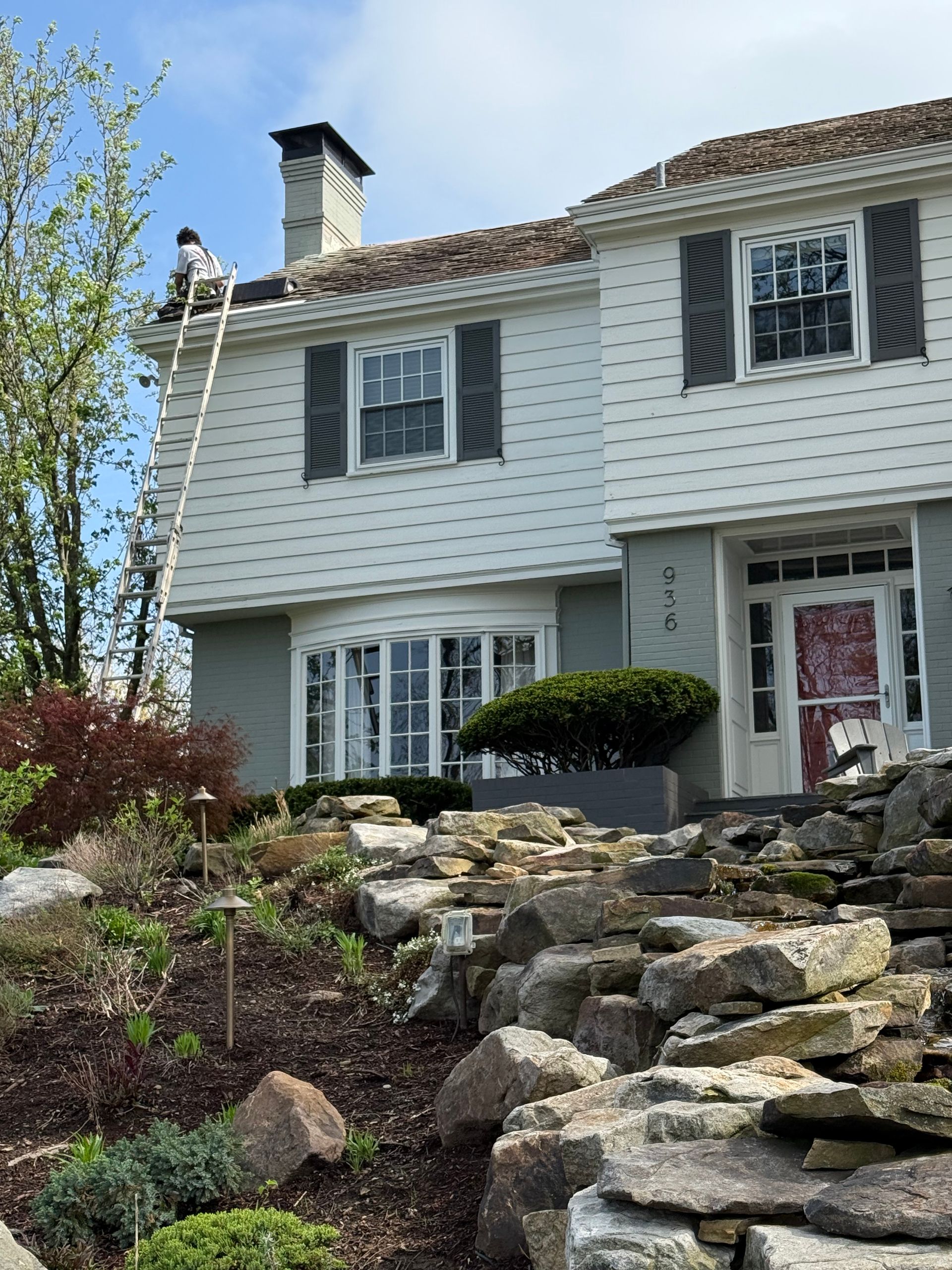 White house with black shutters beside a rocky stone stairway and garden under a clear blue sky