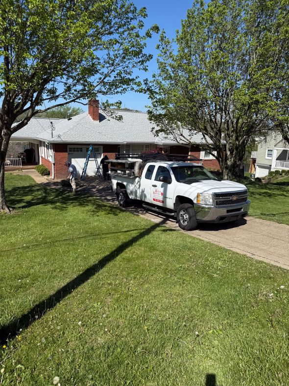 White pickup truck parked in a suburban driveway beside a brick house and green lawn under sunny skies