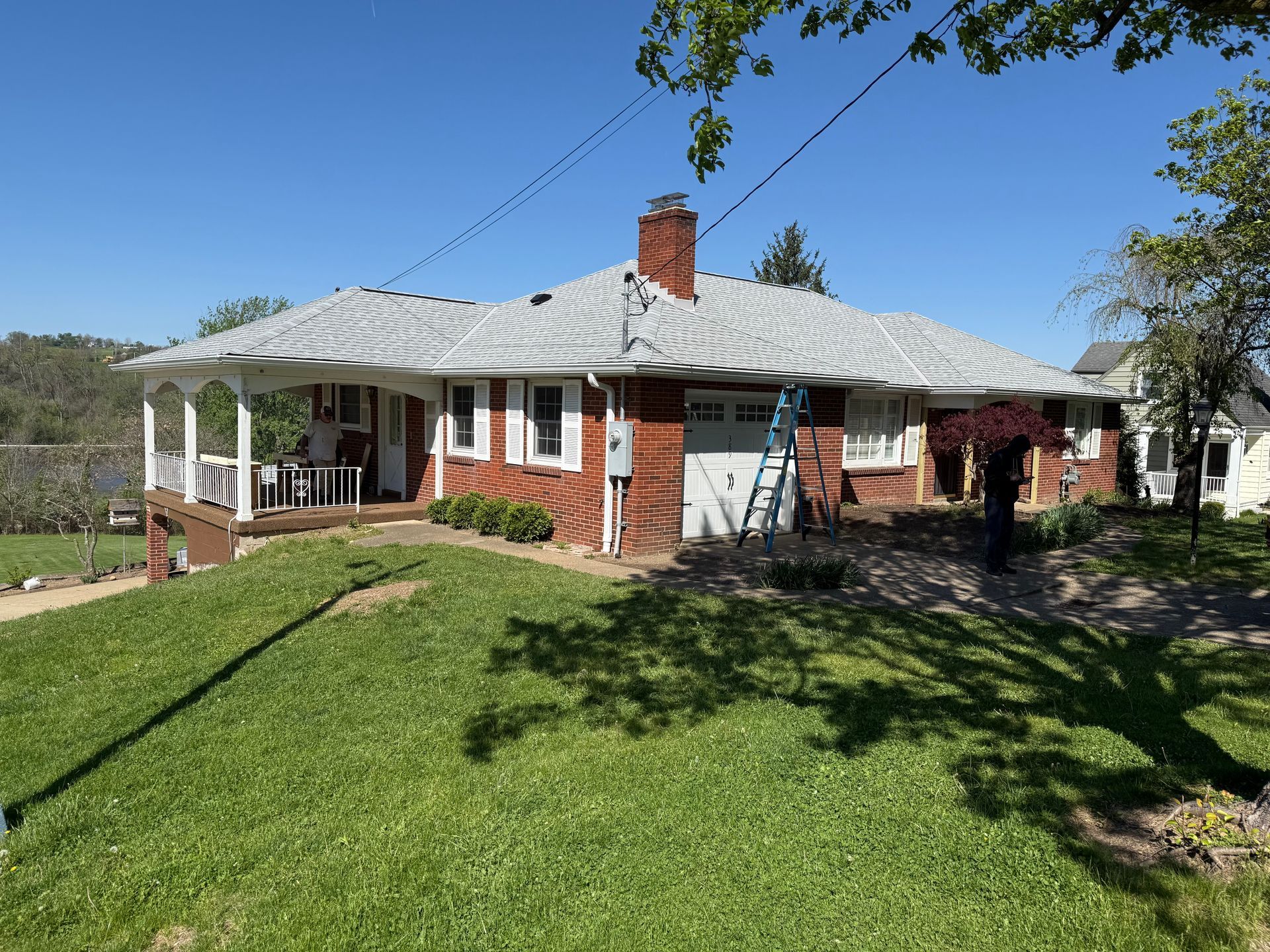 Single-story brick house with white roof, front porch, and a green lawn under a blue sky.