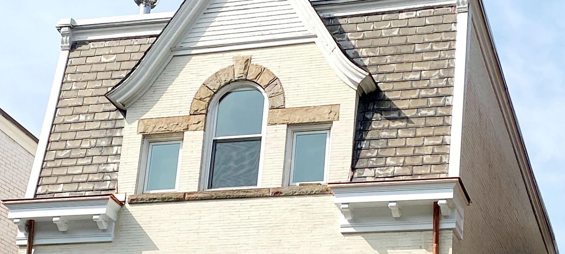Close-up of a house gable with arched window, tan stone trim, and gray shingle siding