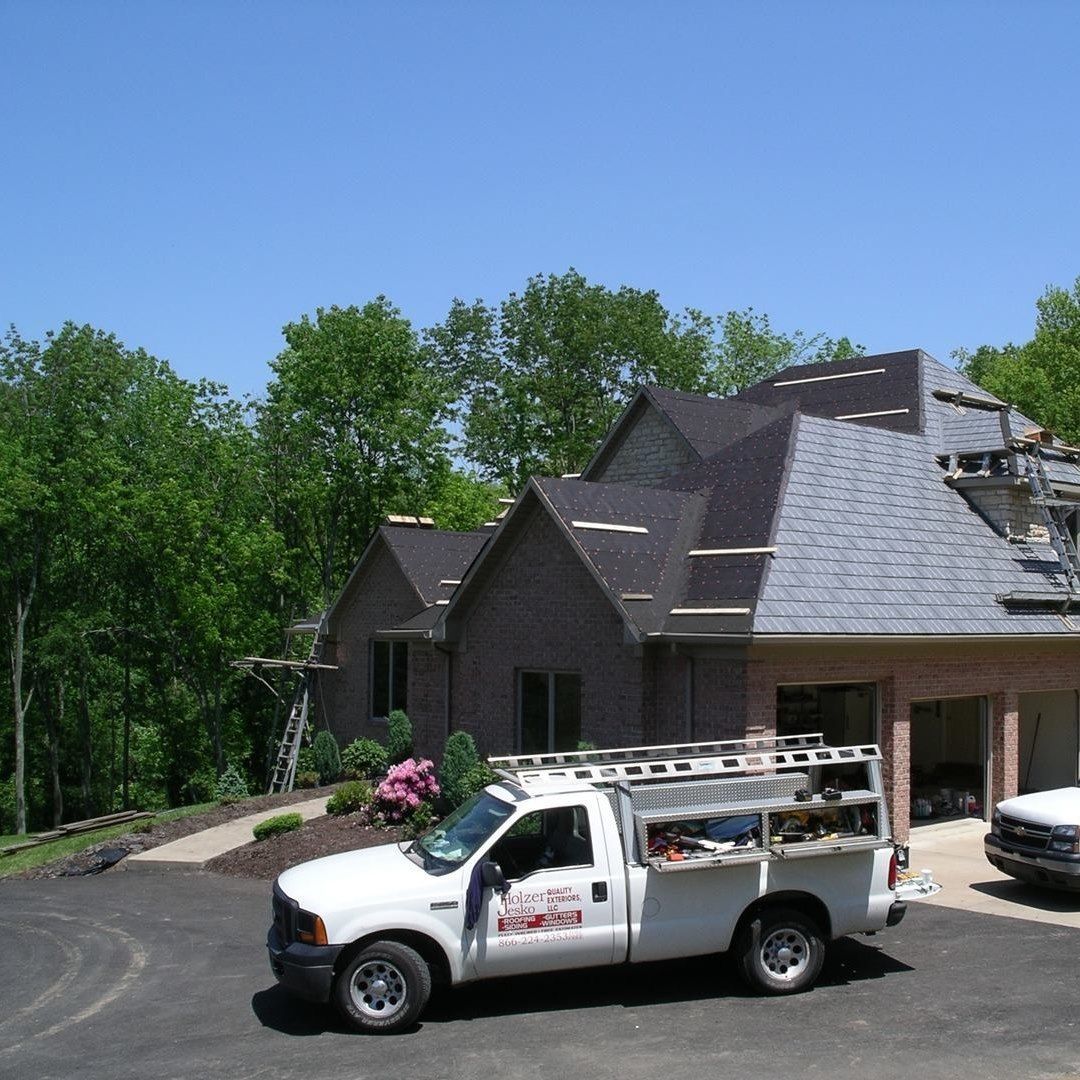 White work truck parked outside a house under construction, with trees and blue sky in the background