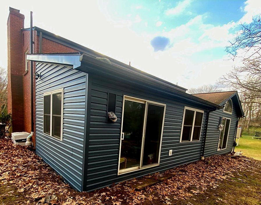 Small blue-gray house addition with sliding glass doors, seen from the yard on a cloudy day