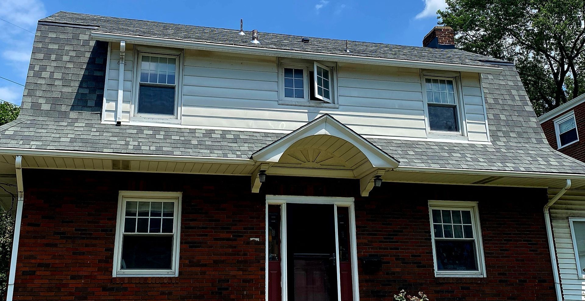 Two-story house with red brick lower level, white siding upper level, and a shingled roof under blue sky